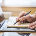 Mãos de redator fazendo anotações estratégicas em caderno sobre notebook focadas em copywriting para seo.