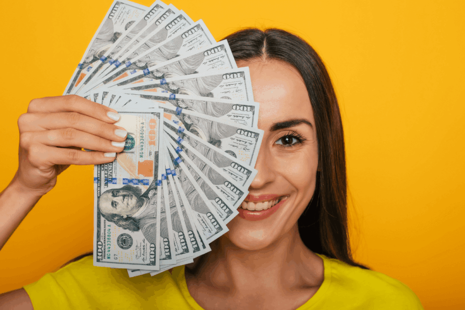 Mulher sorrindo segurando um leque de notas de 100 dólares, ilustrando o resultado financeiro real de quem aprende como fazer micro tarefas na internet.
