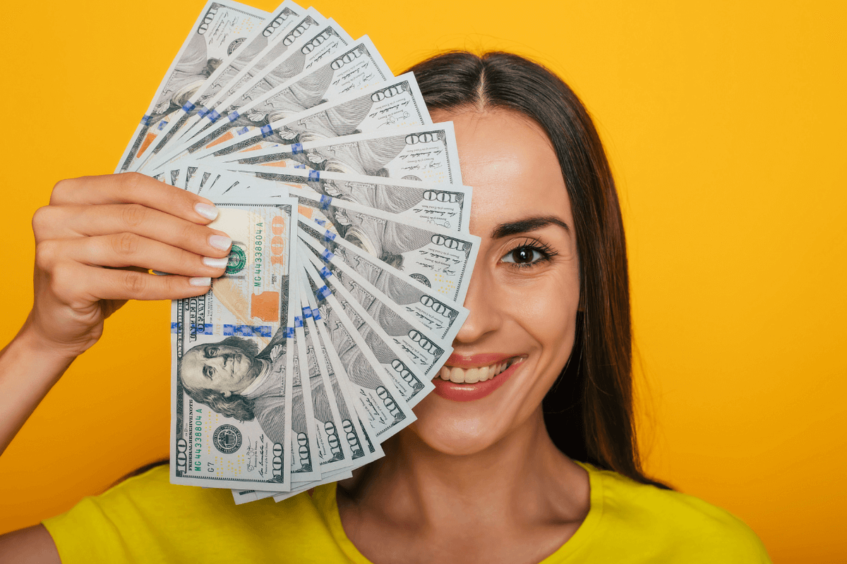Mulher sorrindo segurando um leque de notas de 100 dólares, ilustrando o resultado financeiro real de quem aprende como fazer micro tarefas na internet.