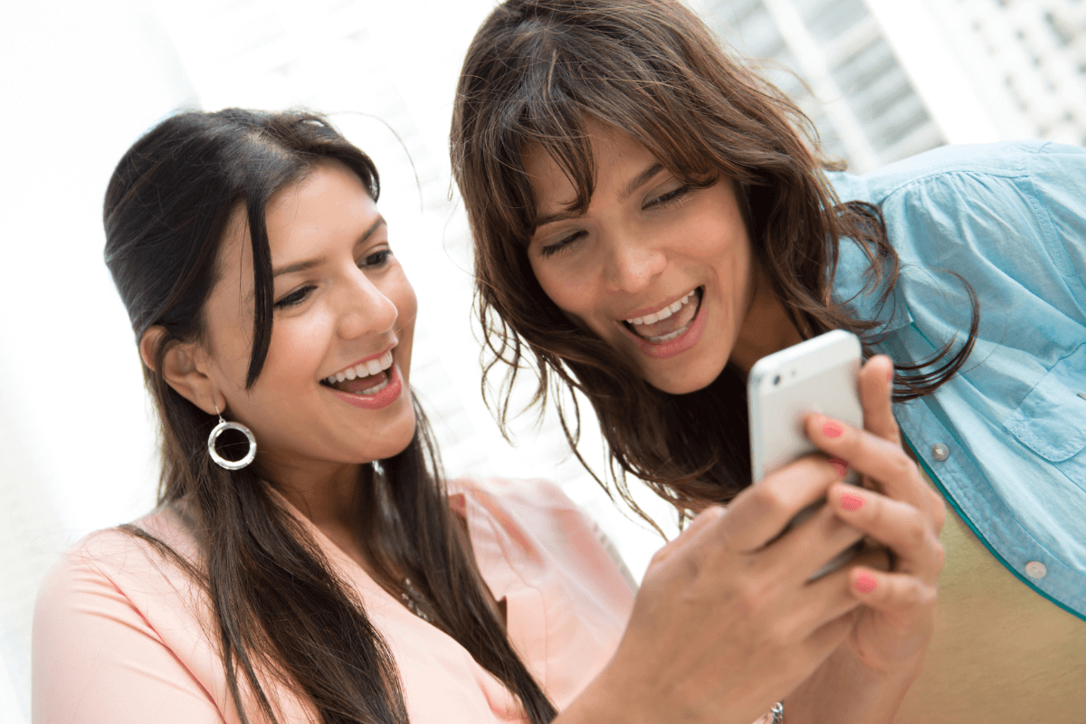 Mulheres sorrindo ao visualizar resultados positivos de crescimento através da visibilidade e estratégias de tráfego orgânico na tela do celular.