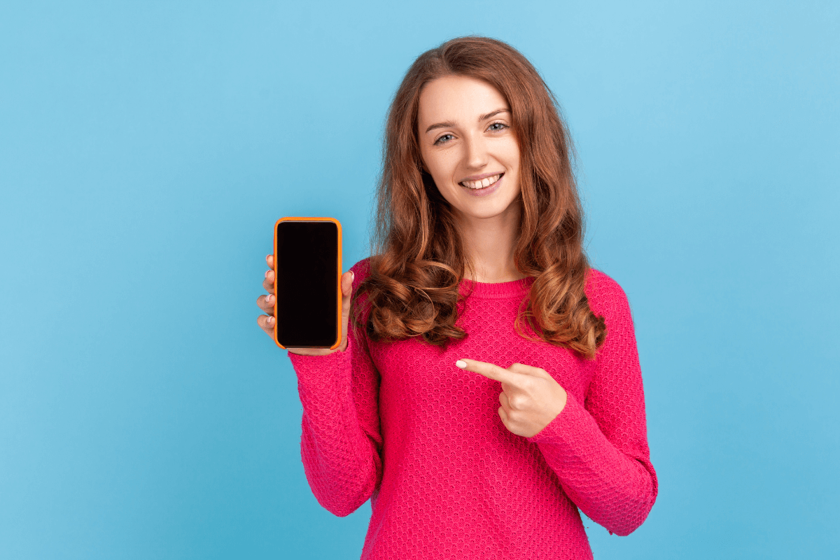 Mulher sorridente apontando para a tela de um smartphone, demonstrando a facilidade de realizar micro tarefas e ganhar dinheiro online usando apenas aplicativos móveis.