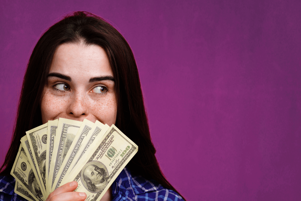 Mulher segurando um leque de notas de cem dólares, ilustrando a estabilidade financeira e os ganhos recorrentes ao trabalhar em projetos de longo prazo com micro tarefas.