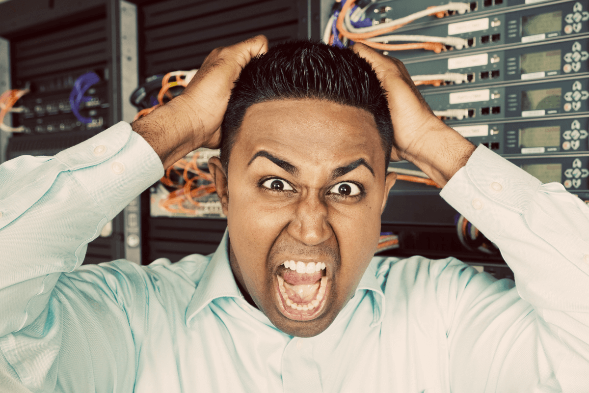 Administrador de sistemas desesperado, gritando e puxando o cabelo em frente a um rack de servidores, ilustrando o estresse causado por falhas críticas, falta de backup e erros de gestão na revenda.