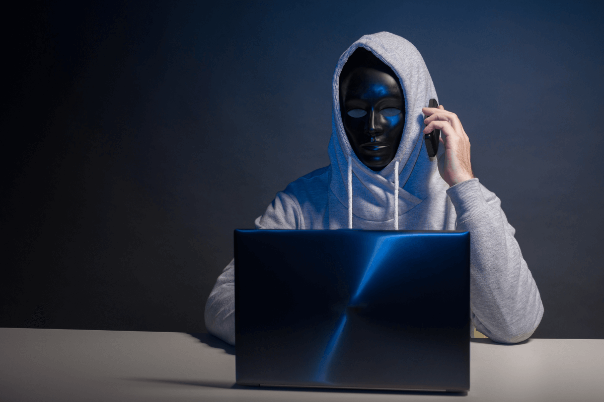 Pessoa com máscara e capuz no computador representando a prevenção contra golpes e fraudes online ao usar o ySense.