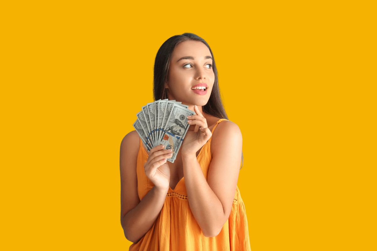 Mulher jovem e sorridente segurando um leque de notas de cem dólares contra um fundo amarelo, ilustrando a satisfação financeira de quem descobre quais as plataformas que estão pagando de verdade na internet.