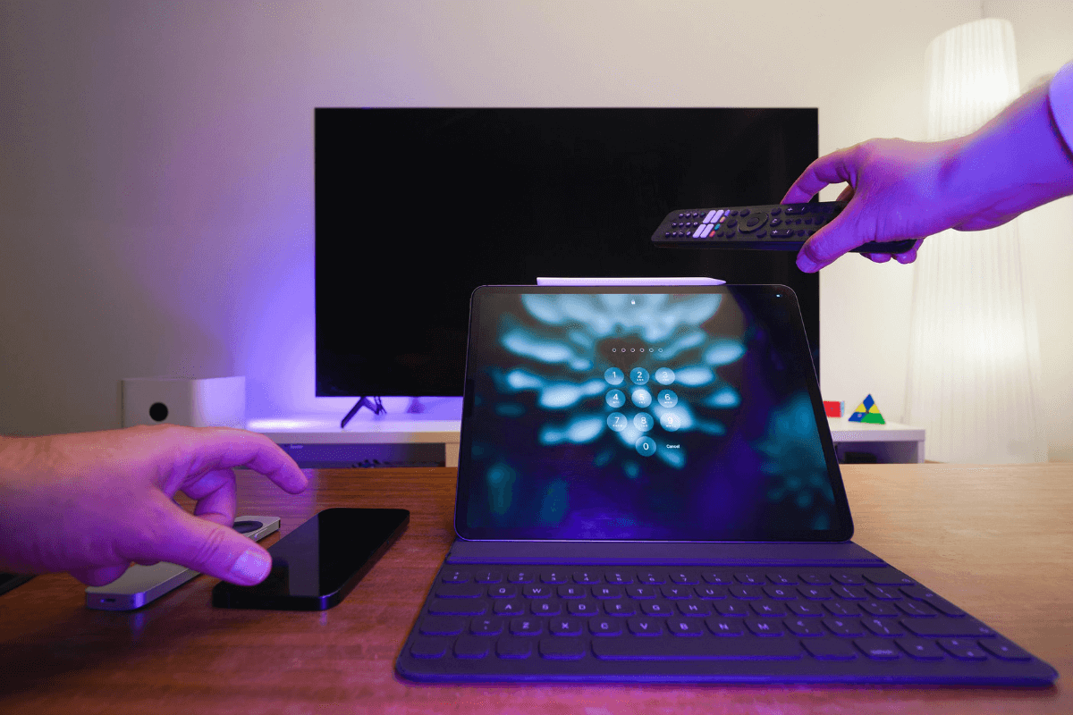 Ambiente tecnológico com tablet exibindo tela de bloqueio com senha e mãos manipulando smartphone e controle, ilustrando a importância de proteger múltiplos dispositivos para garantir segurança digital e prevenção de fraudes ao trabalhar online.